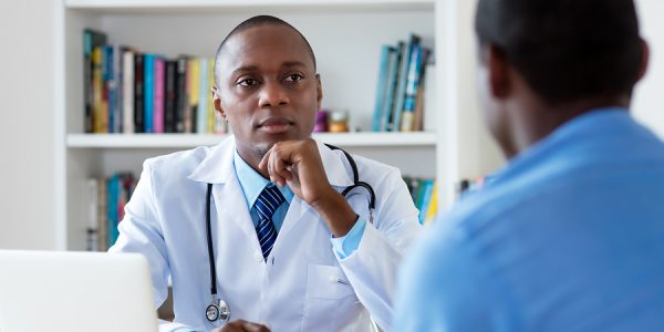 African american doctor listening to problems of male patient at hospital