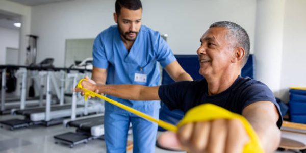 rehabillitation Mature Latin American man doing physical therapy exercises using a stretch band with the assistance of his therapist